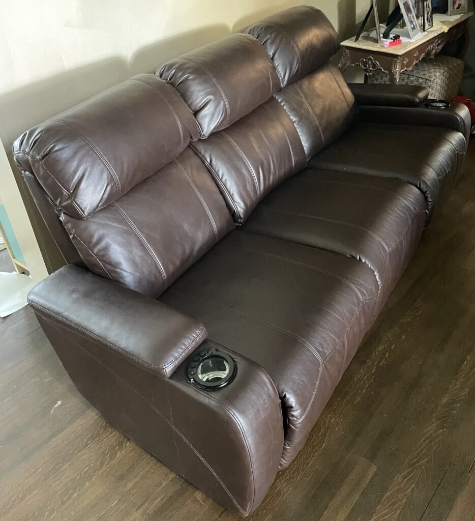 large item pickup brown leather reclining sofa being removed from residential home